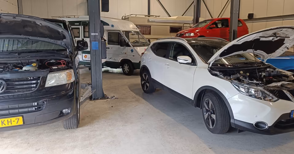 Werkplaats met bestelbus en personenauto met geopende motorkap op de brug